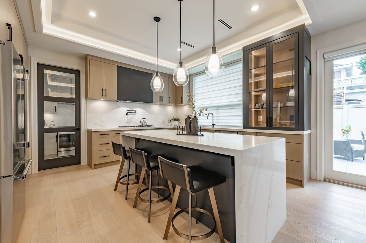 A beautifully remodeled luxury kitchen with white countertops, wooden cabinetry and pendant lighting